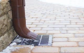 A brown downspout drains water in winter conditions—perfect for discussing Are Rain Chains Better Than Downspouts? with Conifer Gutter Services.