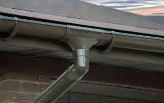 Roof gutter drainpipe installation on house corner, ensuring efficient water flow. Conifer Gutter Services provides expert gutter solutions for your home.