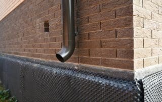 A close-up of a metal downspout, roof gutters downspout installed near unfinished foundation, basement covered with a bitumen waterproofing membrane.
