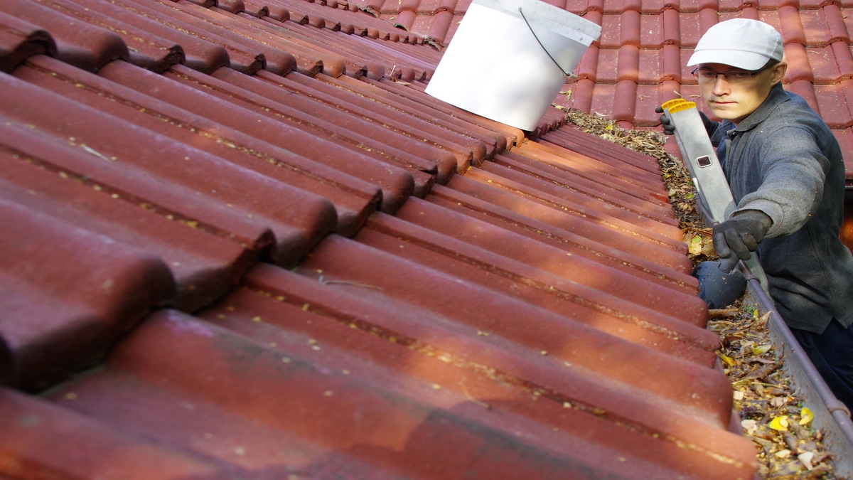 Person cleaning red tile roof gutters.