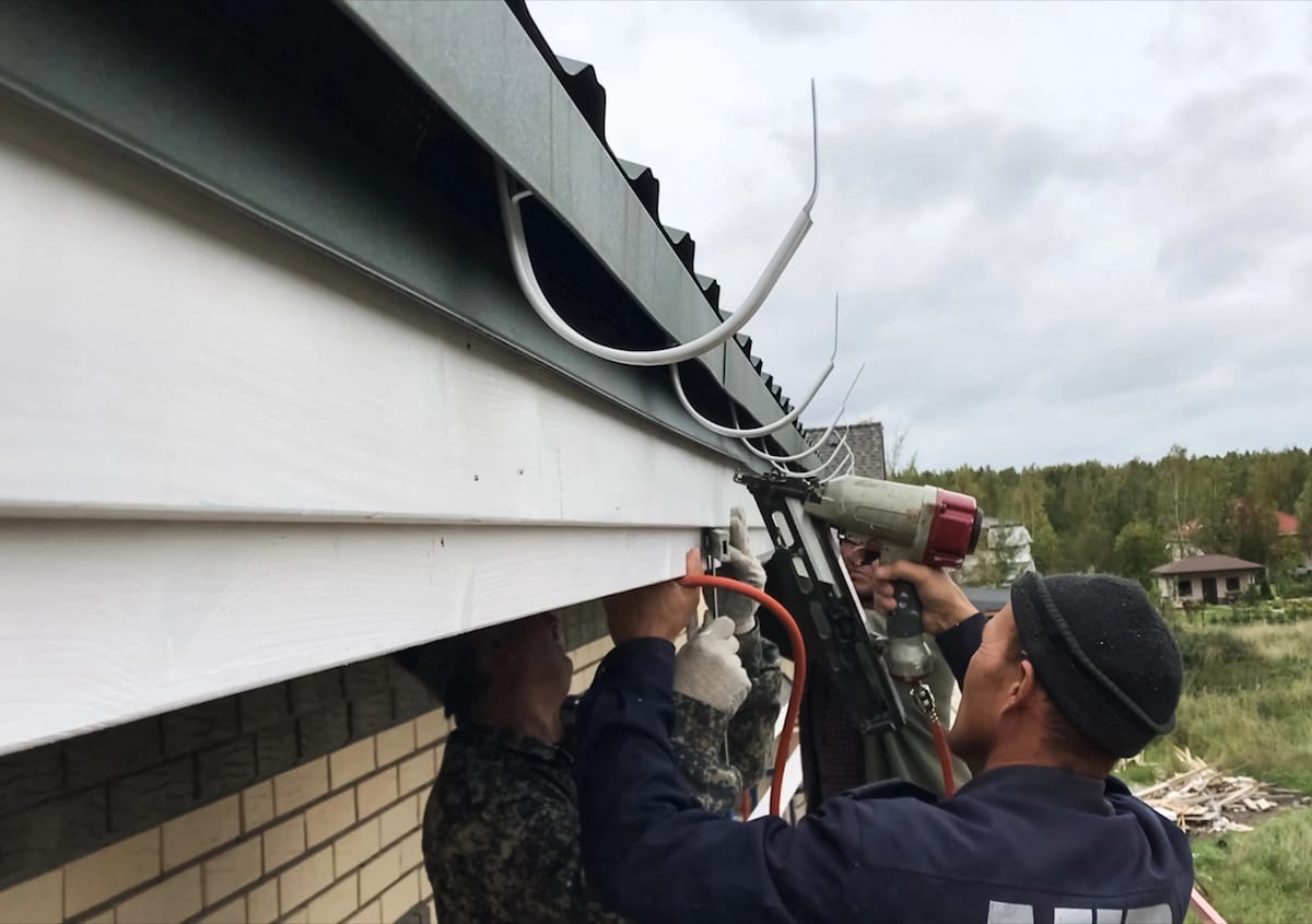 Top Five Things to Consider When Shopping for Gutters Workers installing soffit under roof eaves with nail gun